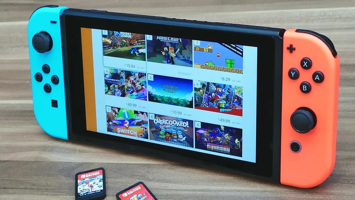 A Nintendo Switch console with a screen displaying a selection of games, accompanied by two game cartridges on a wooden surface.